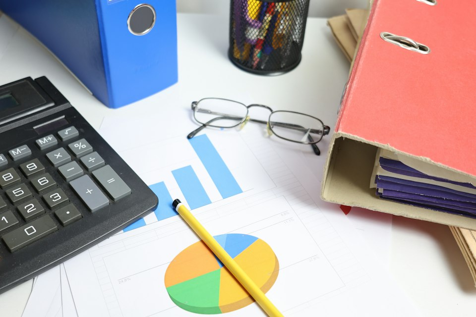 Printed bar and pie charts on a desk beside a calculator, glasses and binders